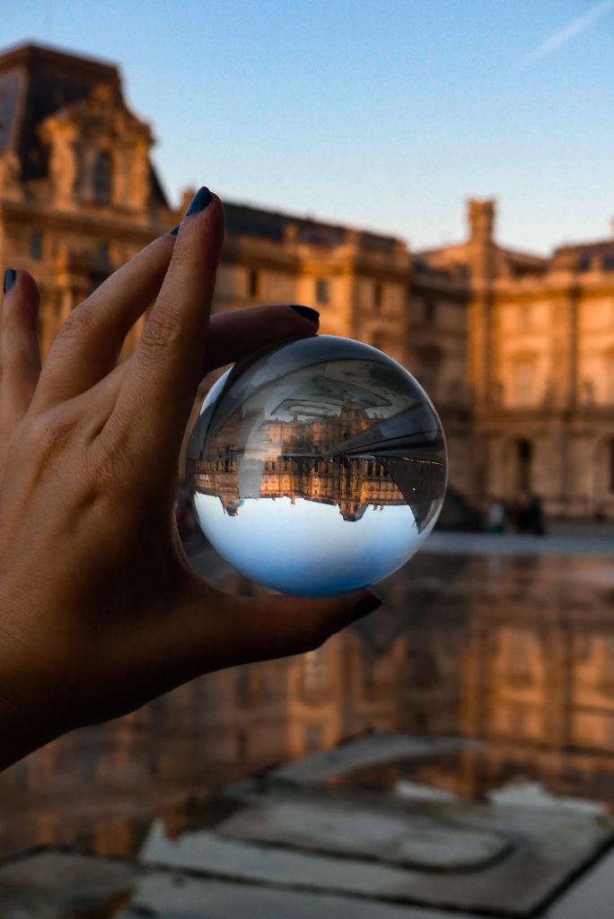 A hand holding a glass ball, with a building in the background. The image of the building in the ball is upside down