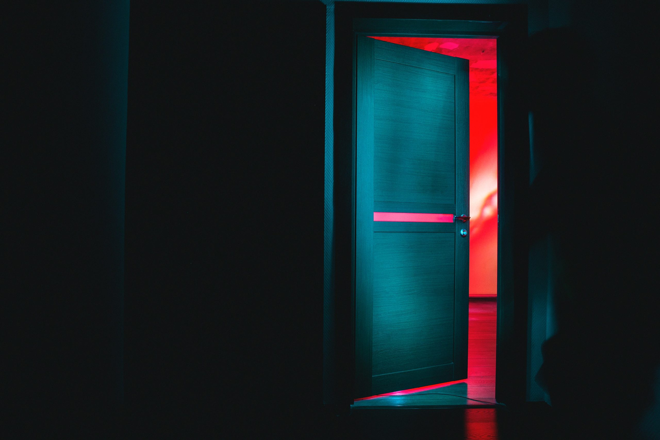 Leicht geöffnete Tür mit Blick in rotes Licht in einem dunklen Raum